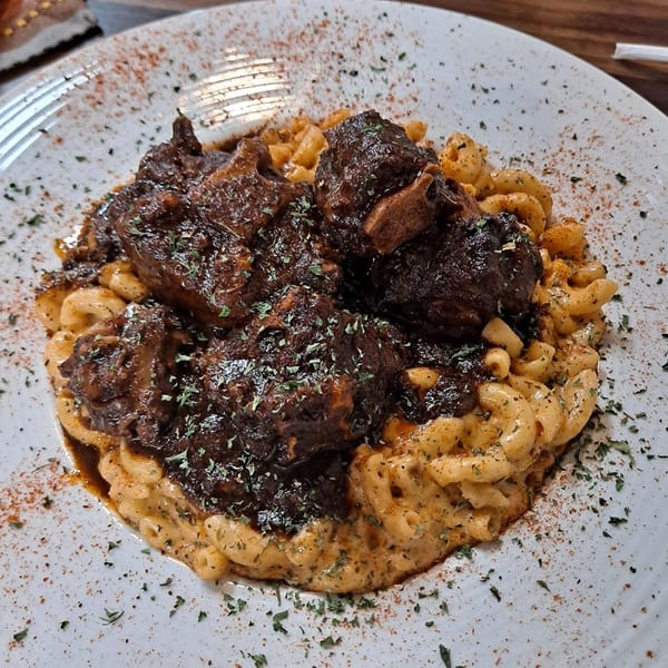 Oxtail and macaroni and cheese, garnished with herbs and spices, on a white plate.