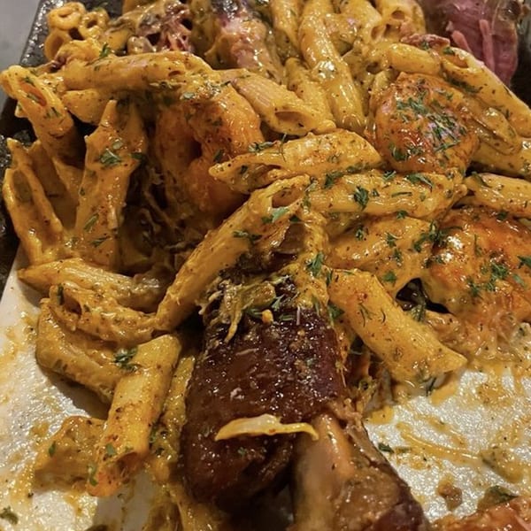 Penne pasta with creamy sauce, herbs, and chicken, with a large piece of meat on the side.